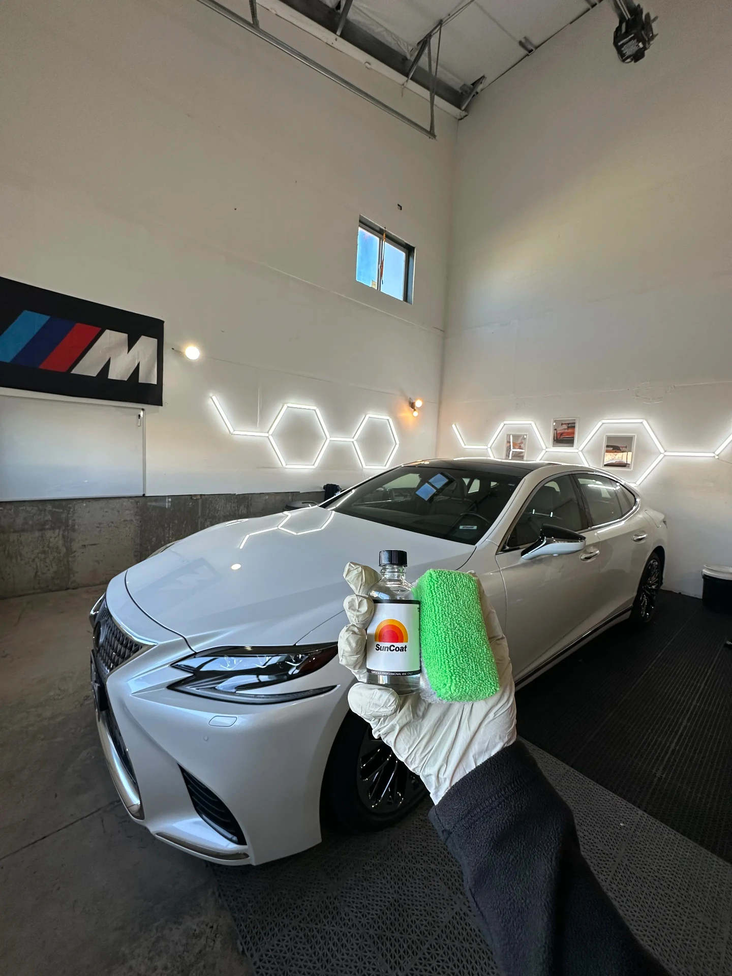 Silver Lexus sedan freshly ceramic coated in the Deluxe Detailing studio, with a bottle of Sun Coat ceramic coating and applicator in hand